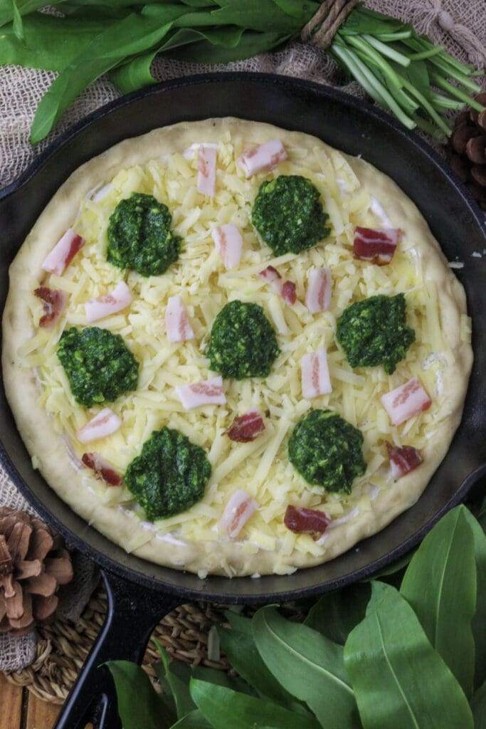 image of pizza dough topped with wild garlic pesto and smoked bacon slices